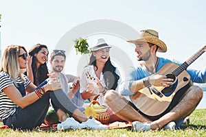 Happy young friends having picnic in the park.They are all happy,having fun,smiling and playing guitar