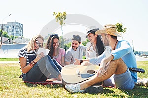 Happy young friends having picnic in the park.They are all happy,having fun,smiling and playing guitar