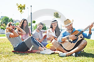 Happy young friends having picnic in the park.They are all happy,having fun,smiling and playing guitar