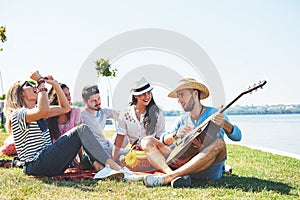 Happy young friends having picnic in the park.They are all happy,having fun,smiling and playing guitar