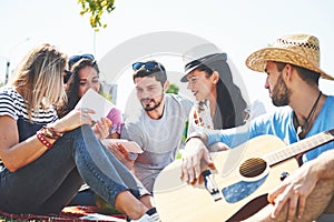 Happy young friends having picnic in the park.They are all happy,having fun,smiling and playing guitar