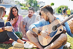 Happy young friends having picnic in the park.They are all happy,having fun,smiling and playing guitar