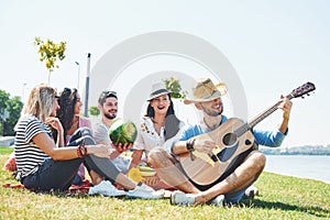 Happy young friends having picnic in the park.They are all happy,having fun,smiling and playing guitar