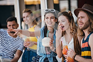 happy young friends holding beverages and looking away while spending time together