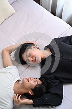 Happy young gay couple lying down on bed, spending time together at home. Concept of sexual freedom and equal rights for