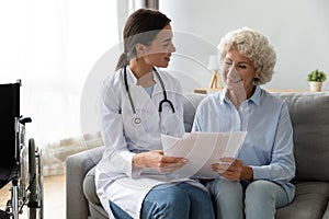 Happy young general practitioner visiting disabled old patient.