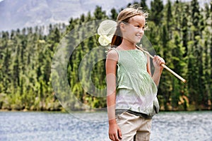 Happy young girl with butterfly net standing by lake