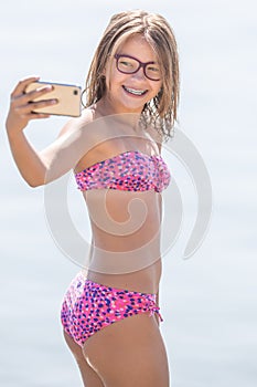 Happy young girl with dental braces making selfhie on beach in summer hot day