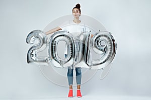 Happy young girl dressed in white t-shirt, jeans and pink socks holding balloons in the shape of numbers 2019 on the