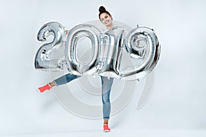 Happy young girl dressed in white t-shirt, jeans and pink socks holding balloons in the shape of numbers 2019 on the