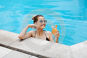 Happy young girl enjoying her refreshing summer cocktail in swimming pool