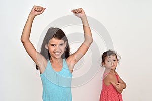 Happy young girl with hands up and her jealous younger  sister