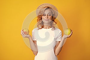 Happy young girl holding apple isolated over yellow background. Portrait of pretty woman with an apple close up.