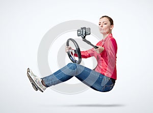 Happy young girl in jeans and a red jacket driving a car and making selfie with a smartphone, on light gray background