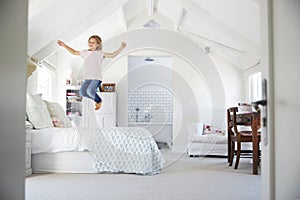 Happy young girl jumping on bed in her bedroom