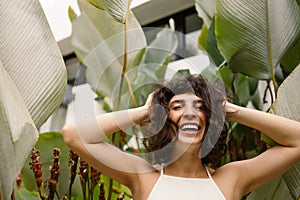 Happy young girl laughing looking at camera holding her head with hands on background of plants.