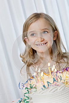 Happy young girl looking away with candles burning on birthday cake