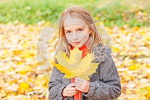 Happy young girl playing with falling yellow leaves in beautiful autumn park on nature walks outdoors. Little child