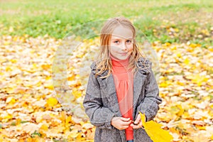 Happy young girl playing with falling yellow leaves in beautiful autumn park on nature walks outdoors. Little child