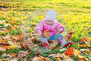 Happy young girl playing under falling yellow leaves in beautiful autumn park on nature walks outdoors. Little child