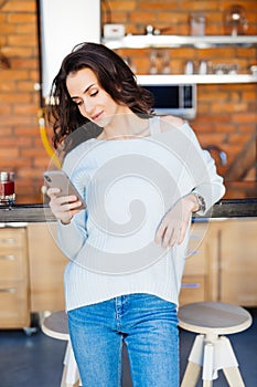 Happy young girl reading a message in a smart phone sitting on a couch at home