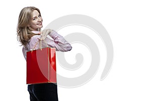 Happy young girl with a red gift bag in her hands. Cute smiling blonde girl wearing a pink shirt and blue trousers. Surprises and