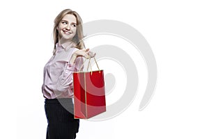 Happy young girl with a red gift bag in her hands. Cute smiling blonde girl wearing a pink shirt and blue trousers. Surprises and