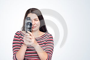 A happy young girl shoots a movie with an old film camera, front view, on a light blue background