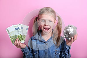 Happy young girl with silver piggy bank and euro banknotes  on pink background. save money concept.