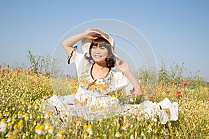 Happy young girl sitting in a flowery meadow in summertime.