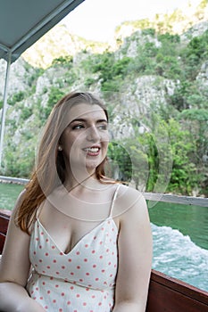 Happy young girl in a small boat smiling with summer clothes. Tourist white skin Woman red head in a canyon enjoying a excursion