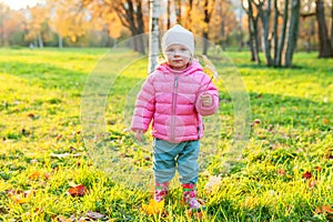 Happy young girl smiling in beautiful autumn park on nature walks outdoors. Little child playing with falling yellow maple leaf in