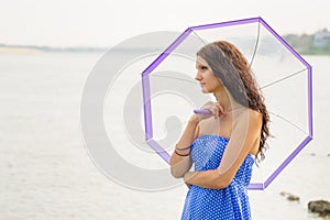 Happy young girl standing with an umbrella on background of a morning river
