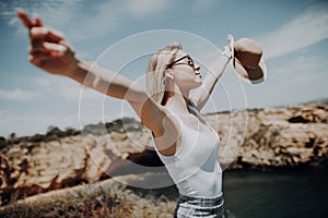 Happy young girl with straw hat is standing on a high and raising her arms up on the ocean view. Summer vocation.