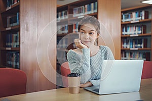 Happy young girl student studying at the college library, sitting at the desk, using laptop computer