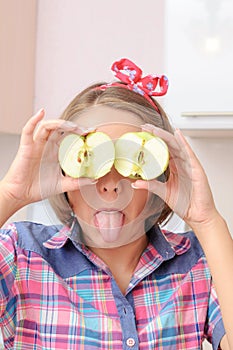 Happy young girl with two apples near her eyes showing her toungue