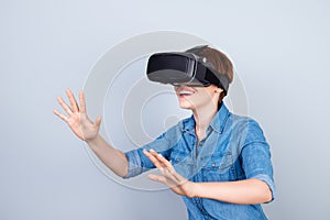 Happy young girl is using vh headset glasses of virtual reality, touching something with her hands like a touch screen