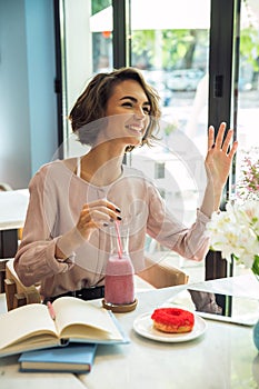 Happy young girl waving hand while drinking smoothie