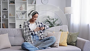 Happy young girl with white headphones chilling and listening her favorite song. African American brunette woman sitting