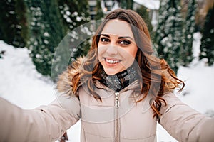 Happy young girl in winter clothes takes selfie on snowy winter background