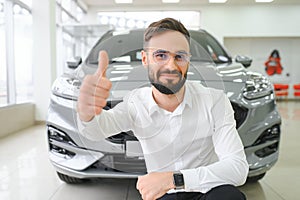 Happy young guy checking new luxury car, buying automobile at dealership centre. Portrait of cheerful millennial