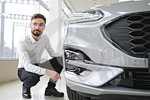 Happy young guy checking new luxury car, buying automobile at dealership centre. Portrait of cheerful millennial