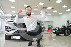 Happy young guy checking new luxury car, buying automobile at dealership centre. Portrait of cheerful millennial