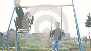 Happy young guy and girl ride on a swing. Outdor. Sunset