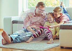 Happy young handsome father having fun with his two cute children playing with tablet