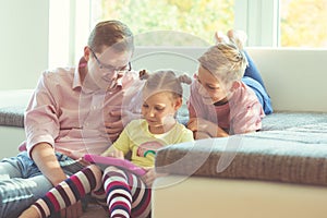 Happy young handsome father having fun with his two cute children playing with tablet