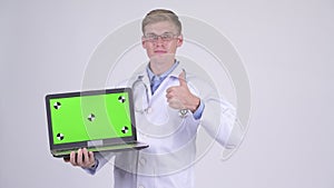 Happy young handsome man doctor showing laptop and giving thumbs up