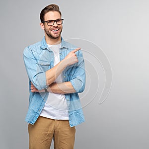 Happy young handsome man in jeans shirt pointing away standing against grey background