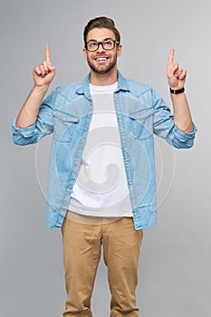 Happy young handsome man in jeans shirt pointing away standing against grey background