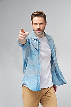 Happy young handsome man in jeans shirt pointing on camera standing against grey background